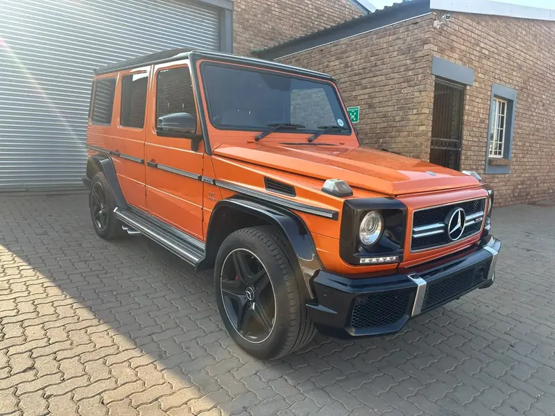 Orange Mercedes-AMG G63 with black wheels and trim, parked outside the workshop